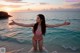 A woman in a pink bikini standing in the ocean with her arms outstretched.