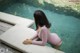 A woman in a pink bodysuit sitting on the edge of a pool.