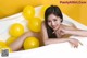 A woman laying in a bathtub with yellow balloons.