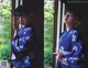 A woman in a blue kimono standing by a window.